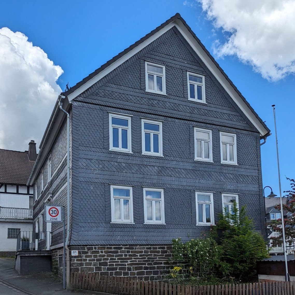 Graues dreigeschossiges Gebäude mit weißen Fenstern und sonnigem Himmel.